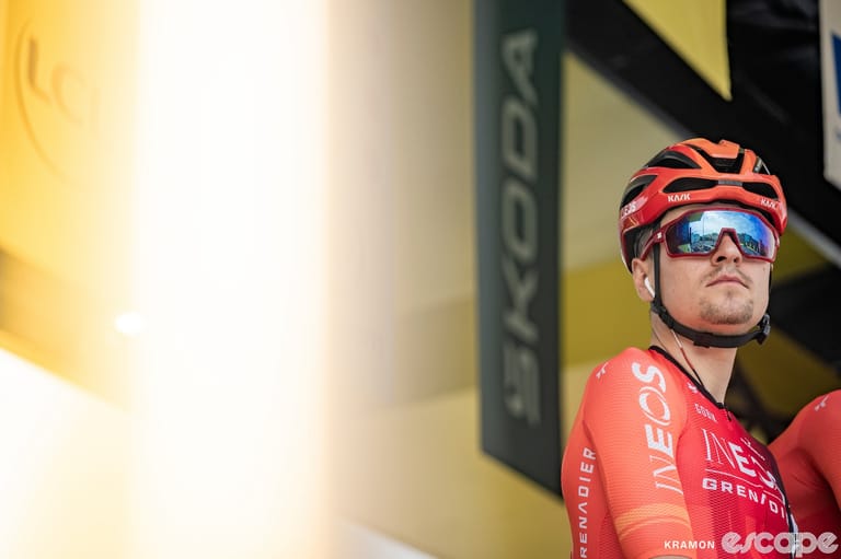 Tom Pidcock stands on a podium at the start of a Tour de France stage. He's alongside his Ineos Grenadiers teammates, but is 