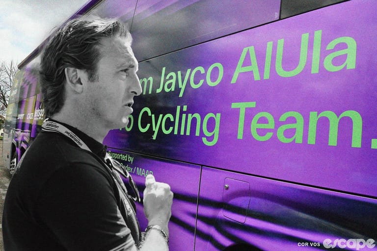 Former Jayco-AlUla director Matt White (in black and white) stands outside the bright purple team bus with a pensive expression.